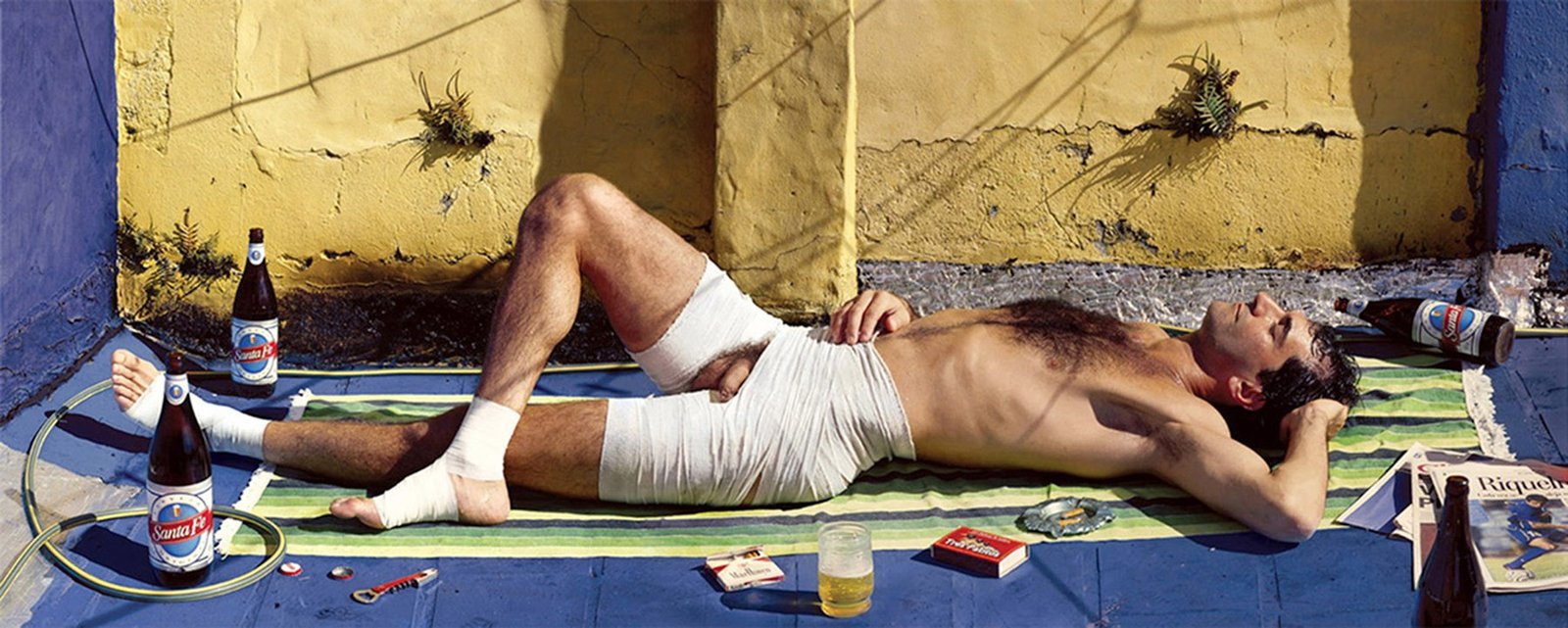 Marcos López: hombre recostado en una terraza con vendas, cerveza y cigarrillos
